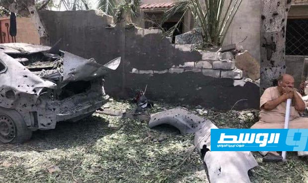 رجل يجلس إلى جوار سيارة دمرت خلال المواجهات في طرابلس