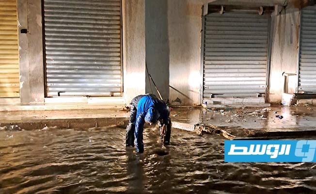 مواطن يحاول فتح بالوعة تصريف مياه أمطار في زوارة، 21 أغسطس 2023. (فيسبوك)