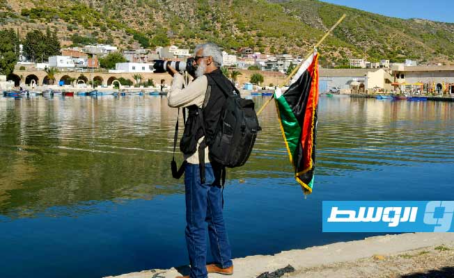 المصور علي الساعدي يحمل علم ليبيا خلال جولة بالميناء العتيق والمعالم الأثرية بغار الملح في بنزرت (الوسط)