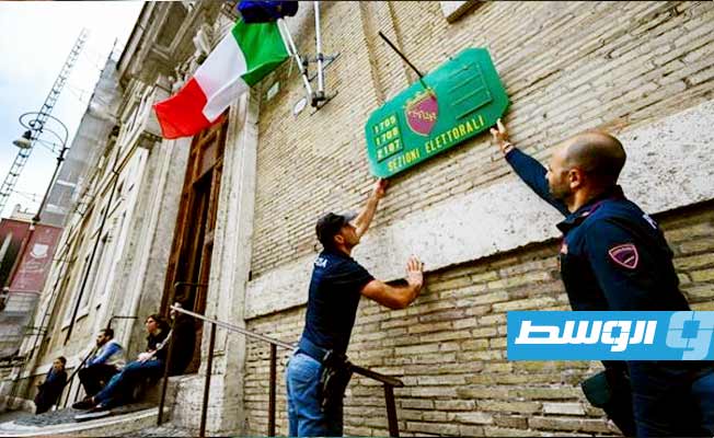 شرطيون يثبتون لافتة تشير إلى مركز اقتراع في روما عشية الانتخابات التشريعية الإيطالية. (أ ف ب)
