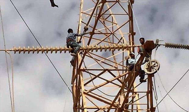 عاملان يغيران أسلاك كهرباء في برج ضغط عالي