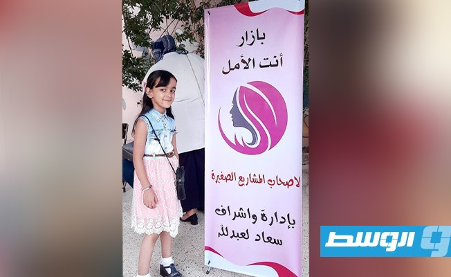 طفلة أمام الملصق الإعلاني لبازار «أنتِ الأمل». (الوسط)