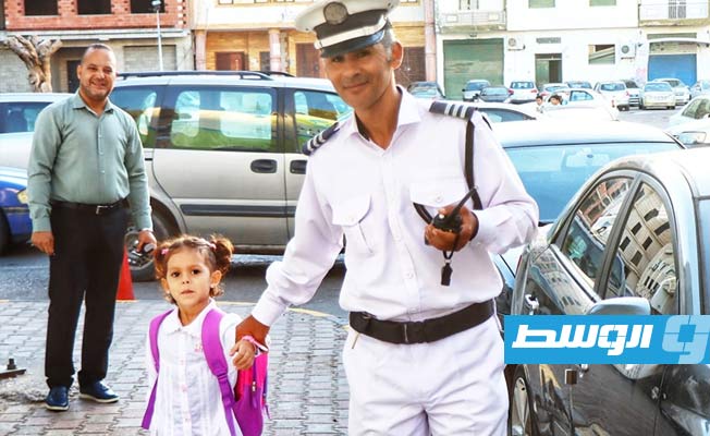 شرطي يساعد تلميذة في عبور الطريق بأحد شوارع العاصمة طرابلس في أول أيام العام الدراسي، 16 أكتوبر 2022. (مديرية أمن طرابلس)