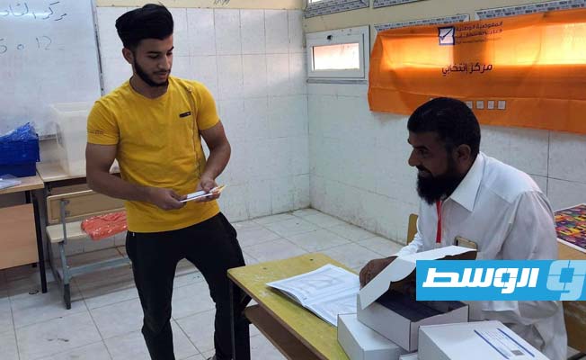 موظف بمكتب الإدارة الانتخابية في أجدابيا يسلم أحد الشباب البطاقة الانتخابية. (الإنترنت)