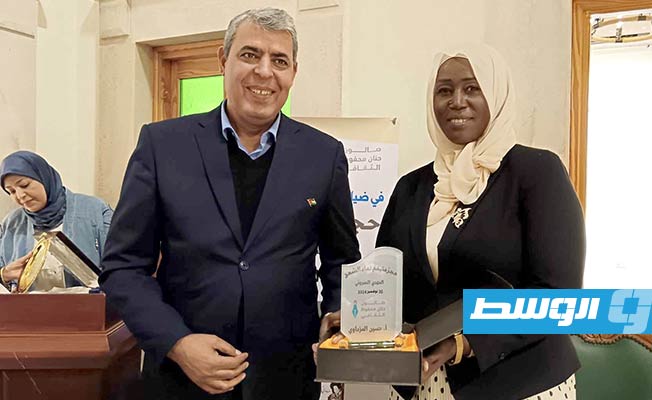 الشاعرة أم الخير الباروني تقدم درع «الإبداع» للكاتب حسين المزداوي. (بوابة الوسط)