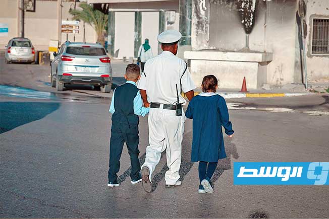 تلميذان يعبران شارع في طرابلس بمساعدة أحد أفراد الشرطة في أول أيام العام الدراسي الجديد، 21 سبتمبر 2025 (مديرية أمن طرابلس)