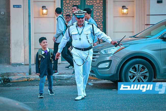 تلميذ يعبر شارع في طرابلس بمساعدة أحد أفراد الشرطة في أول أيام العام الدراسي الجديد، 21 سبتمبر 2025 (مديرية أمن طرابلس)
