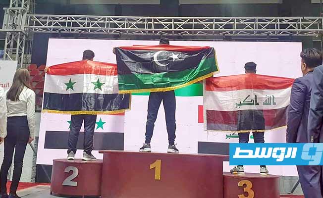 الرباع محمد الشارف الزنتاني يرفع علم ليبيا على منصة التتويج بالمركز الأول في بطولة سورية لرفع الأثفال، 18 يناير 2023. (الإنترنت)