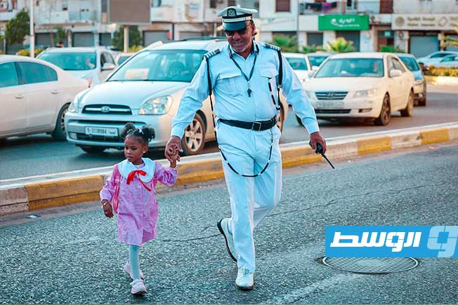 تلميذة تعبر شارع في طرابلس بمساعدة أحد أفراد الشرطة في أول أيام العام الدراسي الجديد، 21 سبتمبر 2025 (مديرية أمن طرابلس)